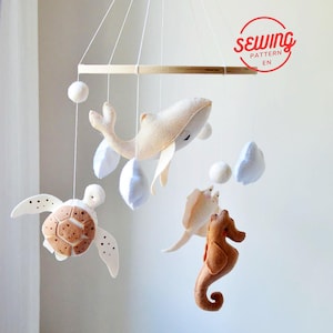 May include: A wooden mobile with felt sea creatures, including a whale, turtle, seahorse, and clouds. The mobile is hanging from a white ceiling.