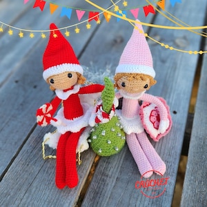 Peut inclure: Deux poupées elfes au crochet faites à la main, une rouge et une rose, avec des bordures et des chapeaux blancs. L'elfe rouge tient un sucre d'orge et l'elfe rose tient un bouclier. Un ornement vert avec des strass est entre eux. Les poupées sont sur une surface en bois.
