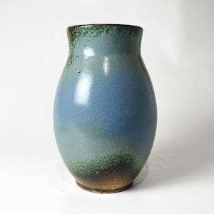 May include: A ceramic vase with a rounded body and a narrow neck. The glaze features a gradient of colours, transitioning from a dark brown base to a mottled green, then a smooth light blue, and finally a dark green rim at the top opening.