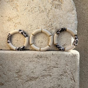May include: Three white bangle bracelets with gold accents. Two bracelets have a black and white animal print design.