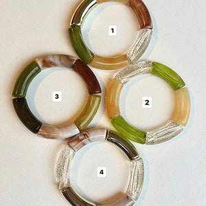 Pu&ograve; includere: Quattro braccialetti colorati realizzati con diversi materiali, tra cui trasparente, marrone, verde e oro. Ogni braccialetto ha un numero da 1 a 4.