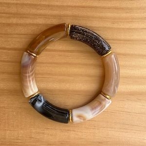 May include: A bracelet made of four different types of stone. The stones are brown, black, white, and a sparkly brown. The bracelet is connected with gold-coloured metal.