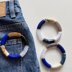 May include: Two colorful bracelets made of white, blue, brown, and black agate stones. The bracelets are on a blue denim background.