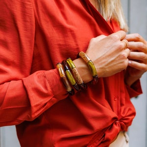 Könnte beinhalten: Ein Set aus vier bunten Armreifen. Die Armreifen bestehen aus einem durchsichtigen Material mit einer gesprenkelten Textur. Die Armreifen sind auf dem Handgelenk einer Person gestapelt.