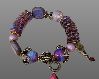 May include: Purple and iridescent glass bead bracelet with a gold charm and a pink crystal pendant. The bracelet has a tag that says "Natalie Bosquin".