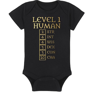 May include: Black baby bodysuit with gold text. The text reads "LEVEL 1 HUMAN" above a list of stats: STR 2, INT 4, WIS 4, DEX 3, CON 3, and CHA 20. The bodysuit has short sleeves and a snap closure.
