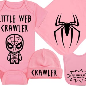 May include: A pink baby gift set featuring a bodysuit with "LITTLE WEB CRAWLER" and a Spider-Man graphic, a matching beanie with "CRAWLER", a bib with "my cape's on backwards", and a blanket with a black spider design.