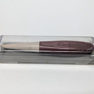 Puede incluir: Primer plano de un dedal de costura de plástico marrón y blanco en una caja de plástico transparente. El dedal tiene el texto "Talla Extra Pequeña" impreso en él.