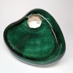 May include: A green ceramic heart-shaped dish with a hole in the center. The bottom of the dish is signed "Laurie 1961".