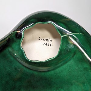 May include: A green ceramic bowl with a hole in the bottom. The bowl is signed "Laurie 1961" on the inside.