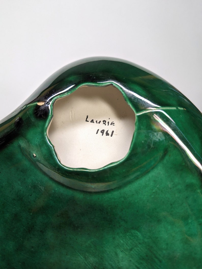 May include: A green ceramic bowl with a hole in the bottom. The bowl is signed "Laurie 1961" on the inside.