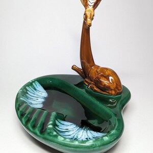 May include: A green ceramic ashtray with a deer figurine on top. The ashtray has two compartments and white accents.