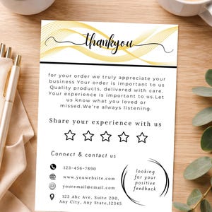 Op de afbeelding: Een witte kaart met het woord "thankyou" in script, een gouden golfontwerp en zwarte tekst. De kaart bevat contactgegevens, een verzoek om feedback en een vijfsterrenbeoordelingssectie. De kaart ligt op een houten oppervlak.
