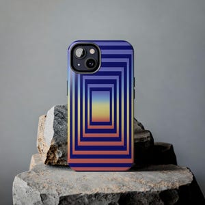 May include: A smartphone case with a geometric design. The case features a series of nested rectangles in shades of blue, orange, and yellow. The phone case is resting on a rough, gray stone.