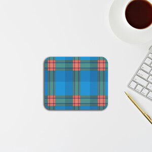 May include: A square coaster featuring a blue, teal, and coral plaid pattern with rounded corners. The design consists of a grid of intersecting horizontal and vertical lines in varying shades of blue and teal, accented by small coral squares.
