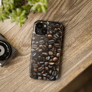 May include: A clear phone case with a design of brown coffee beans. The case is designed for a phone with a triple lens camera.
