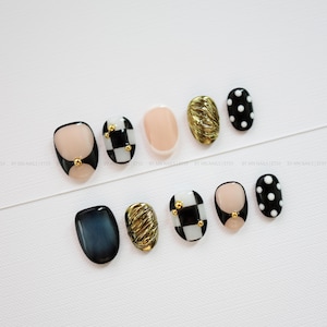 Puede incluir: Un conjunto de diez uñas postizas con varios diseños, incluyendo patrones de cuadros blancos y negros con tachuelas doradas, uñas color nude, uñas doradas metálicas texturizadas, uñas negras con lunares blancos y uñas azul oscuro efecto ojo de gato.
