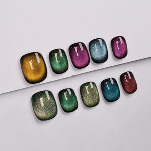 Op de afbeelding: Tien kleine, ronde, magnetische nagellak kleuren. De kleuren zijn goud, groen, paars, blauw, rood, groen, goud, blauw, groen en rood.