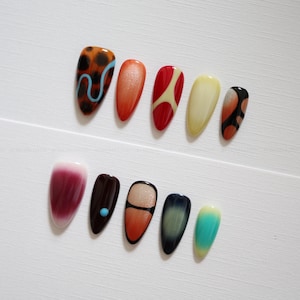 Puede incluir: Un conjunto de diez uñas postizas en forma de almendra con diseños variados que incluyen carey con una línea ondulada azul claro, naranja sólido, rojo con detalles en crema, amarillo pálido, marrón oscuro con un punto azul y varios degradados.