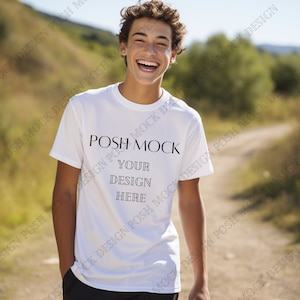 Puede incluir: Una camiseta blanca con el texto "POSH MOCK" y "YOUR DESIGN HERE" impreso en la parte delantera. La camiseta la lleva puesta una persona al aire libre.
