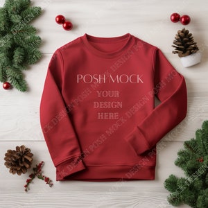 May include: Red crewneck sweatshirt mockup with the text "POSH MOCK YOUR DESIGN HERE" on a white wood background with pine branches and red ornaments.