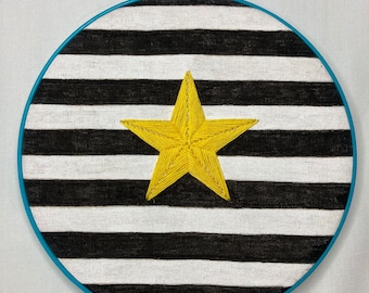 Hand Made Wall Art. Yellow Star embroidered on a black and white fabric framed in a blue hoop.