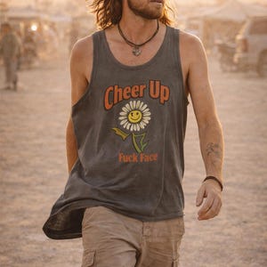 May include: A gray tank top with the words "Cheer Up" and "Fuck Face" printed on it, along with a smiling daisy graphic. The person is wearing a baseball cap, sunglasses, and cargo shorts.