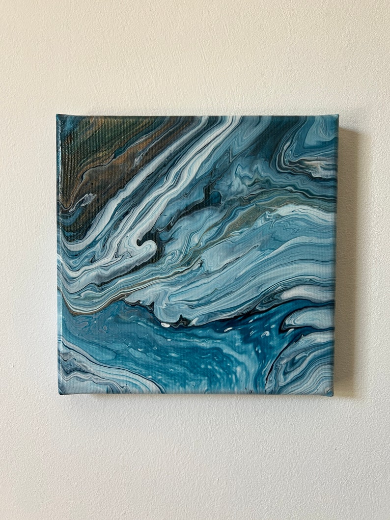Puede incluir: Pintura abstracta sobre lienzo con colores azules, blancos y grises que se arremolinan. La pintura tiene un aspecto fluido y org&aacute;nico, que recuerda al agua o las nubes.