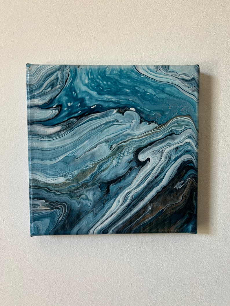 Puede incluir: Pintura abstracta sobre lienzo con pintura azul, blanca y negra que se arremolina creando un efecto de m&aacute;rmol.