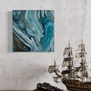 Puede incluir: Pintura abstracta con pintura azul, blanca y dorada en espiral. La pintura est&aacute; enmarcada y colgada en una pared blanca. Un barco modelo y un par de binoculares est&aacute;n en primer plano.