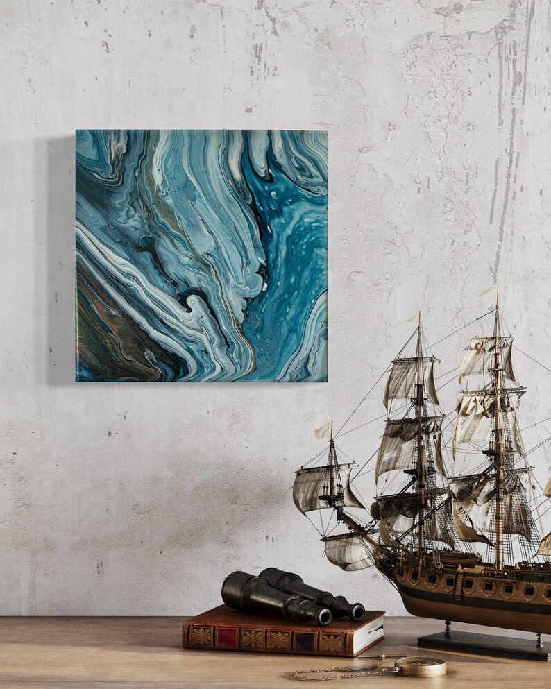 Puede incluir: Pintura abstracta con pintura azul, blanca y dorada en espiral. La pintura est&aacute; enmarcada y colgada en una pared blanca. Un barco modelo y un par de binoculares est&aacute;n en primer plano.