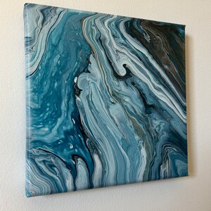 Puede incluir: Pintura abstracta sobre lienzo con colores azules, blancos y grises que se arremolinan. La pintura tiene un aspecto fluido y org&aacute;nico.