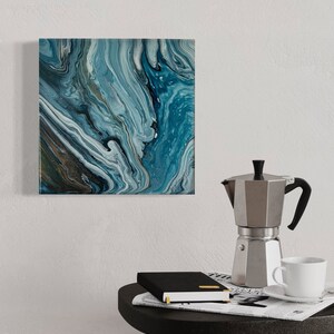 Puede incluir: Una pintura abstracta cuadrada con pintura azul, blanca y gris en espiral. La pintura est&aacute; colgada en una pared blanca sobre una mesa auxiliar negra con una cafetera, una taza y un platillo, y un cuaderno negro encima de un peri&oacute;dico.