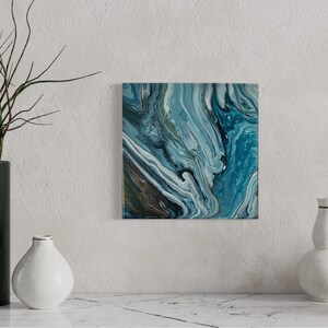 Puede incluir: Pintura abstracta con pintura azul, blanca y dorada en espiral. La pintura tiene una superficie texturizada y est&aacute; enmarcada en un marco blanco.