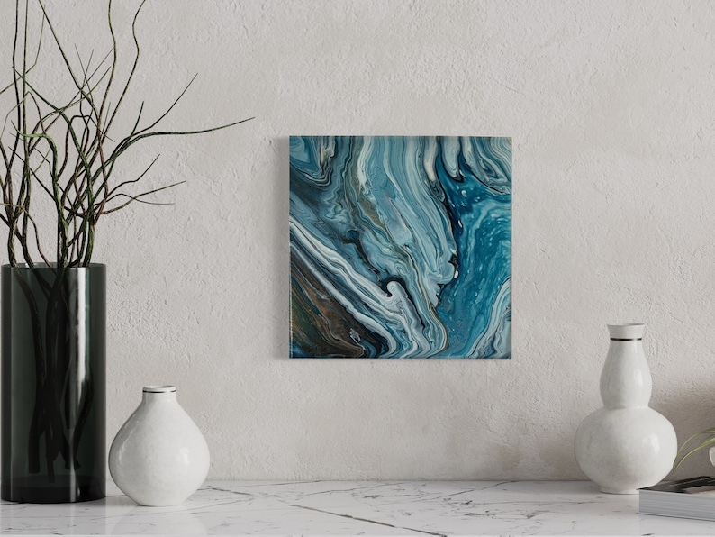 Puede incluir: Pintura abstracta con pintura azul, blanca y dorada en espiral. La pintura tiene una superficie texturizada y est&aacute; enmarcada en un marco blanco.
