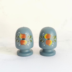 May include: Two blue wooden salt and pepper shakers. Each shaker has a rounded top and a pedestal base. The shakers are decorated with a floral design in orange, yellow, and green. The shakers are approximately 3 inches tall.