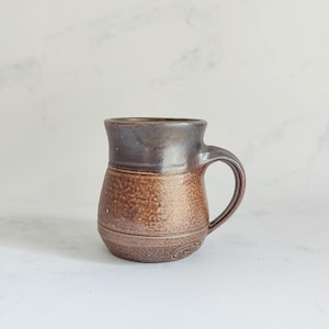 May include: A white ceramic mug with a black handle and the text "But First, Coffee" in a black, handwritten-style font. The mug is on a white surface.