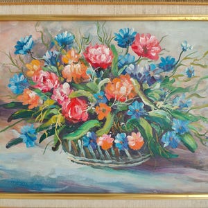 May include: Oil painting of a floral arrangement in a basket, framed in gold. The flowers are a mix of red, orange, and blue, with green leaves. The background is a soft, muted color.