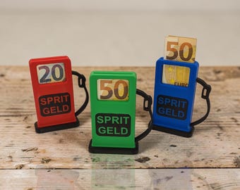 Puede incluir: Tres pequeñas réplicas de surtidores de gasolina de plástico en rojo, verde y azul, cada uno con una manguera negra y una ventana. El surtidor rojo muestra el número 20, el verde 50 y el azul contiene un billete de 50 euros. Todos tienen el texto SPRIT GELD.