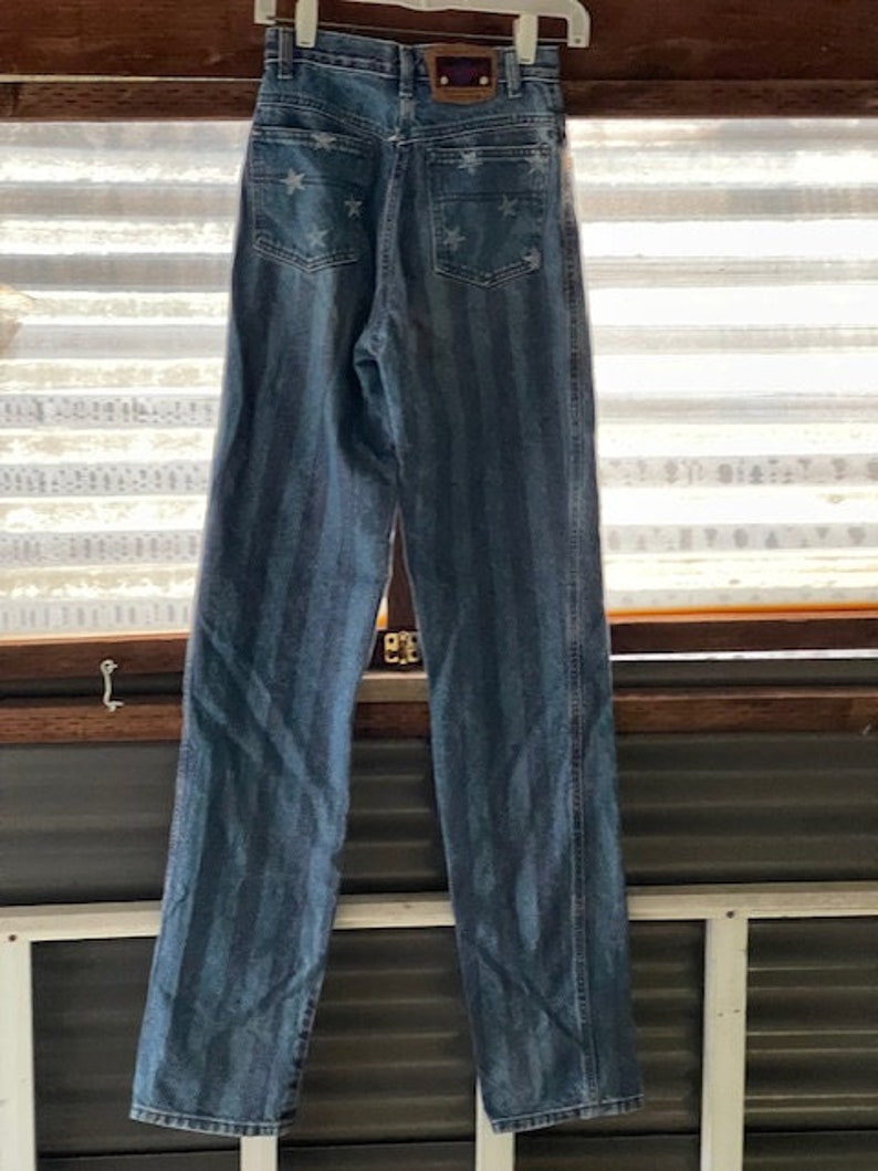 May include: A pair of blue denim jeans with white stars and vertical stripes. The jeans have a high waist and a straight leg.