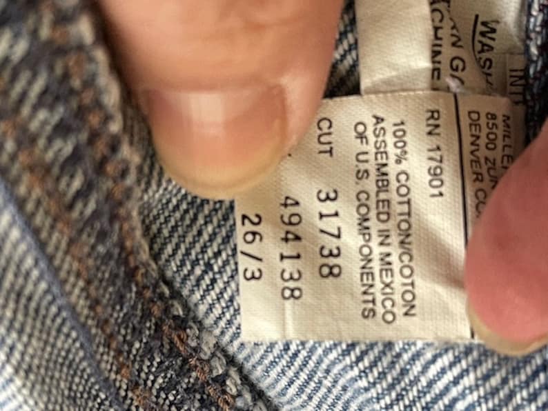 May include: A white tag with black text that reads "100% Cotton/Coton Assembled in Mexico of U.S. Components Cut 31738 494138 26/3 RN 17901 WASH/INT 8500 ZUN DENVER CO. ANG CHINE"
