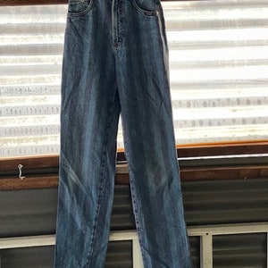 May include: A pair of blue denim jeans with a white stripe down the side seams. The jeans are hanging on a white hanger.