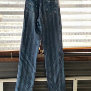 May include: A pair of blue denim jeans with white stars and vertical stripes. The jeans have a high waist and a straight leg.