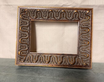 May include: A rectangular, ornate picture frame with a dark brown finish and gold accents. The frame features a detailed, repeating scroll design around the edges. The frame is empty, ready for a photo or artwork.