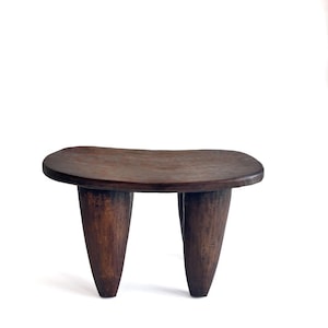Peut inclure: Un tabouret en bois brun foncé à trois pieds avec un dessus arrondi. Les pieds sont coniques et se rétrécissent vers la base. Le tabouret est en bois massif et foncé et a un aspect naturel et rustique.