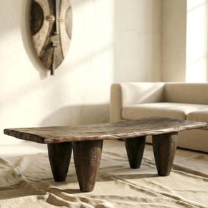 Op de afbeelding: Een rustieke, rechthoekige salontafel van donkerbruin, verweerd hout. De tafel heeft een dik, ongelijkmatig blad en wordt ondersteund door drie stevige, kegelvormige poten. De tafel is ongeveer 152 cm lang.