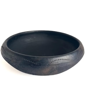 Puede incluir: Un pequeño cuenco de cerámica negro con una superficie texturizada ligeramente rugosa. El cuenco tiene una forma simple y redondeada y un borde ligeramente acampanado.