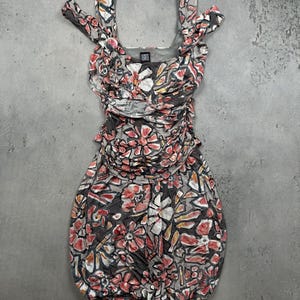 May include: A sleeveless dress featuring a gray base with a multi-colored floral and geometric pattern in shades of red, white, and orange. The garment has a ruched bodice, wide shoulder straps, and a bubble-style hemline with a Liz Claiborne label.