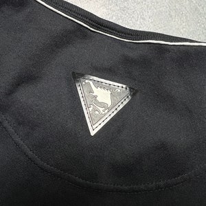 May include: Black t-shirt with a white trim around the neckline. A silver triangle-shaped patch with a design is sewn onto the back of the shirt.