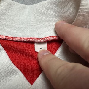 Puede incluir: Primer plano de un cuello de camisa blanco y rojo. El cuello es blanco, con el interior rojo. La etiqueta de talla muestra la letra "L". La camisa est&aacute; hecha de una tela suave y texturizada.